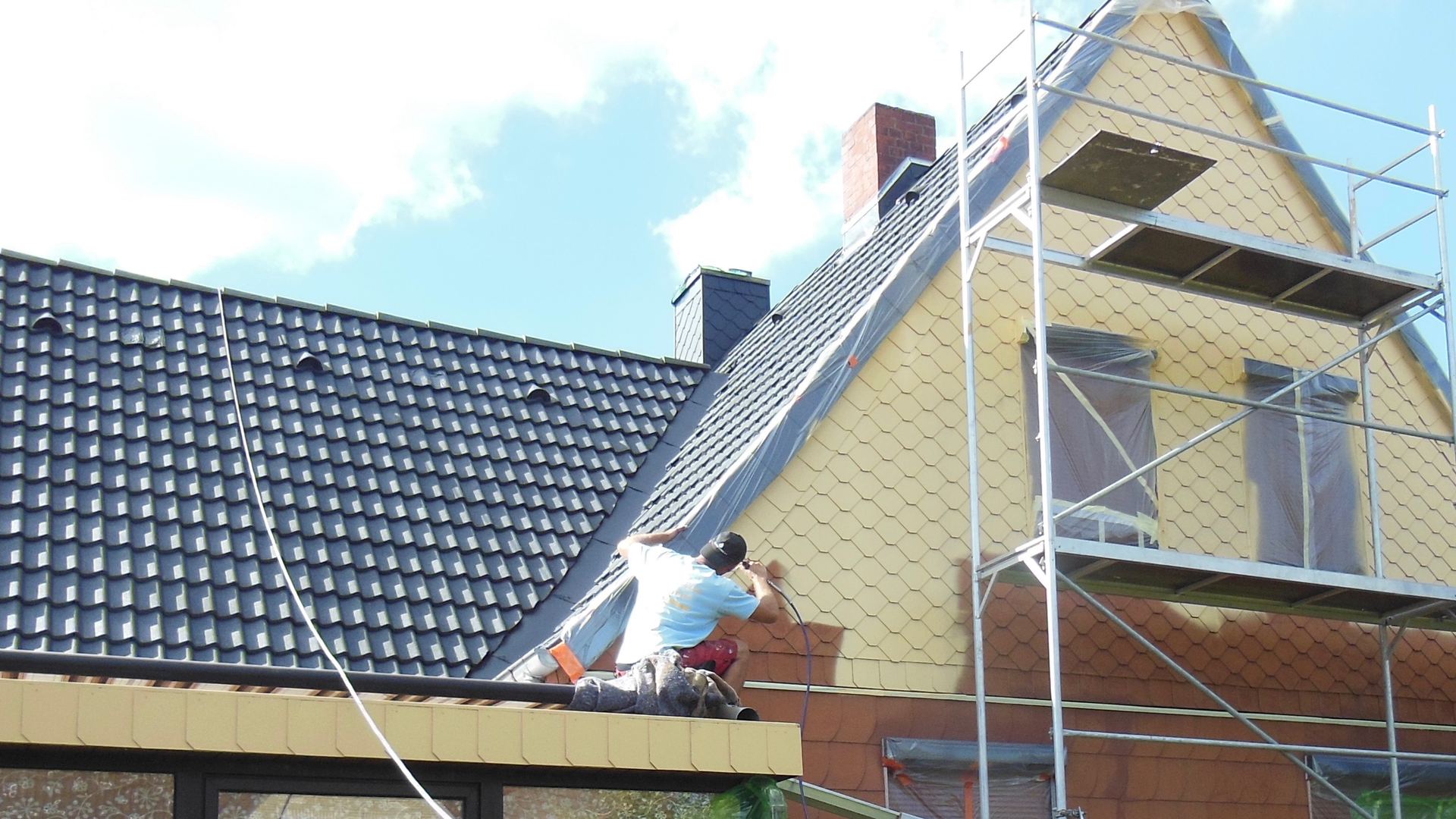 Giebel mit Fassadenplatten wird beschichtet, Fenster mit Folie abgeklebt, Gerüst an der Wand