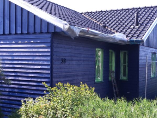 Holzhaus mit dunkelblau gestrichener Schalung, Dachrand mit Folie abgedeckt