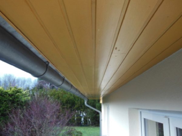Frisch gestrichene helle Dachuntersicht aus Holz über einer weißen Hauswand mit Regenrinne