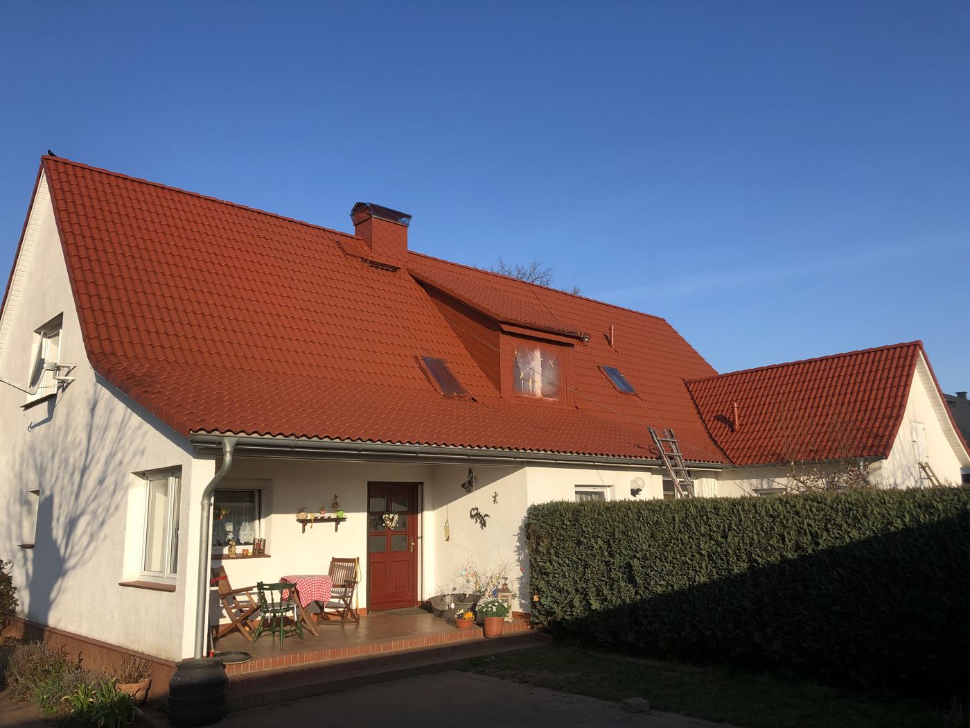 Einfamilienhaus mit frisch beschichtetem roten Dach, Dachrinne, weißer Fassade und Terrasse